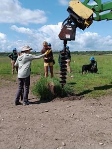 A group of people watch someone drill into mud.