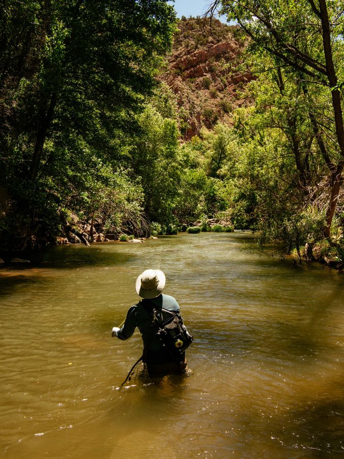A man wades through knee deep water in a desert river