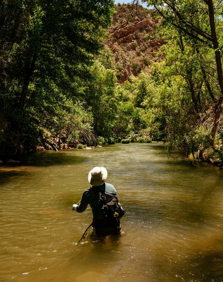 A man wades through knee deep water in a desert river