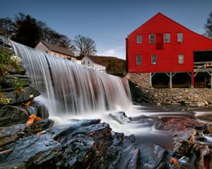 A small waterfall near an old red mill building.