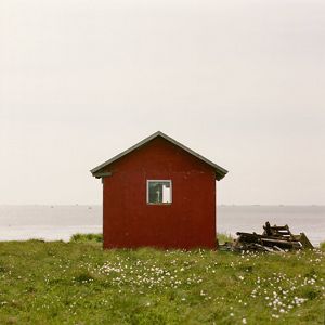 Red house with window in green field on edge of water