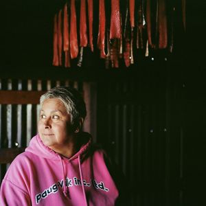 woman in sweatshirt below hanging red strips of fish