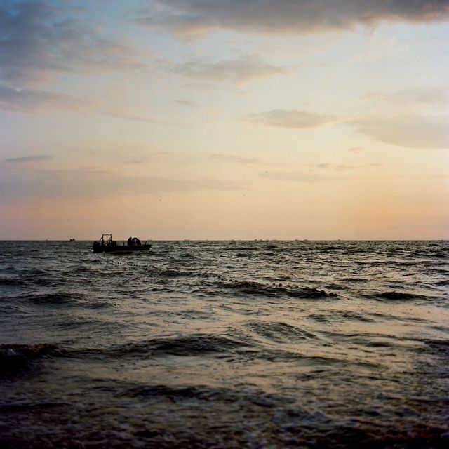 a small boat is silhouetted on water with waves, sky is sunset colored, no land on horizon