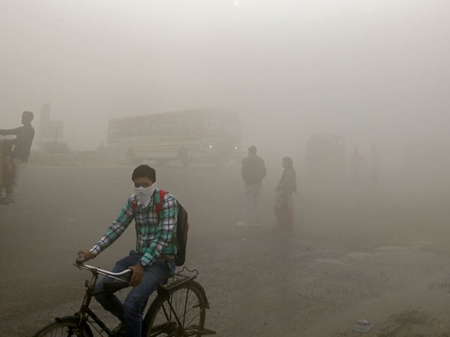 Indian commuters walk and bike through smog on the outskirts of New Delhi