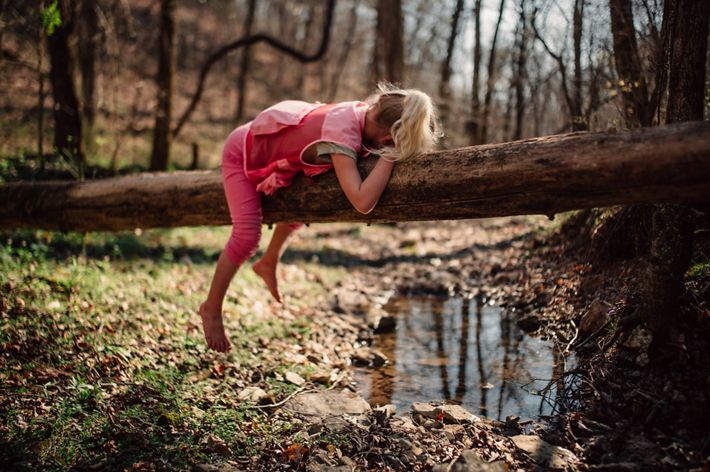 A girl lies facedown on a log over a creek.