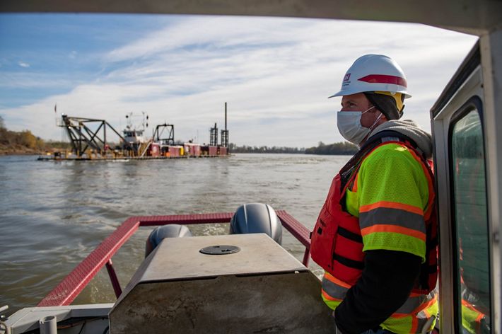 A man in construction gear watches dredging equipment.