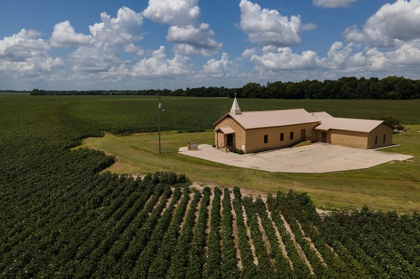 A small church is surrounded closely by agricultural fields.