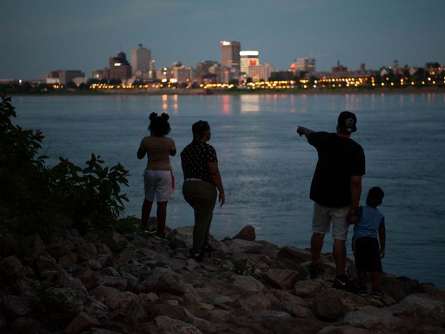 A family stands by the river at twilight, looking across the river at the Memphis skyline.