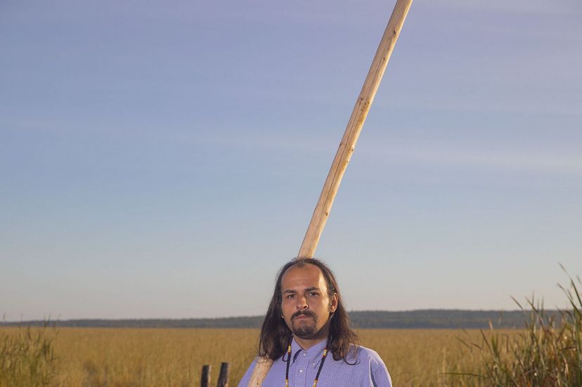 A man stands near a canoe with a long pole used to push it through the water.