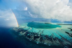 A rainbow ends at an aquamarine atoll