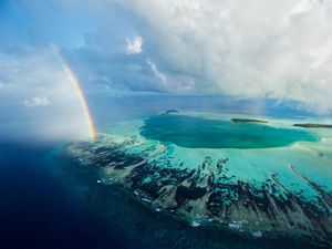 A rainbow ends at an aquamarine atoll
