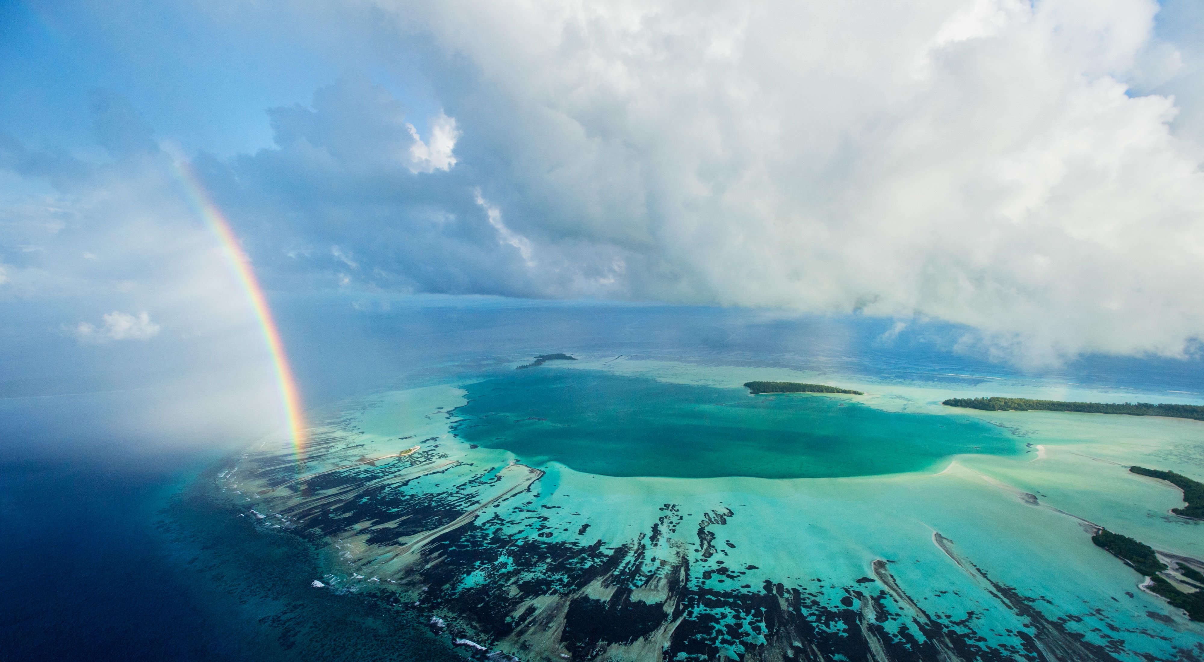 A rainbow ends at an aquamarine atoll