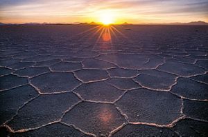 wide shot of grey ground with many hexagon shapes in the dirt leading to a sunset on a horizon