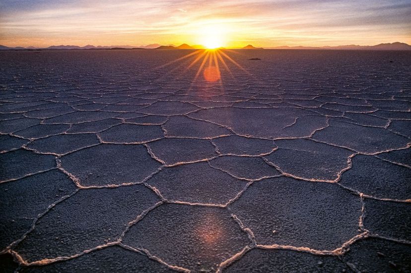 wide shot of grey ground with many hexagon shapes in the dirt leading to a sunset on a horizon
