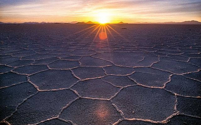 wide shot of grey ground with many hexagon shapes in the dirt leading to a sunset on a horizon