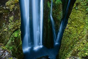 blue water falls in a waterfall between two green moss-covered rock walls