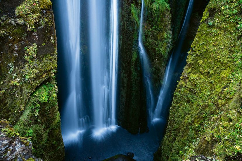 blue water falls in a waterfall between two green moss-covered rock walls