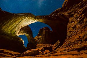 two rock arches are seen, lit against a clear starry night sky