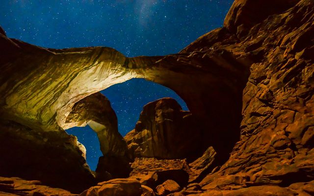two rock arches are seen, lit against a clear starry night sky