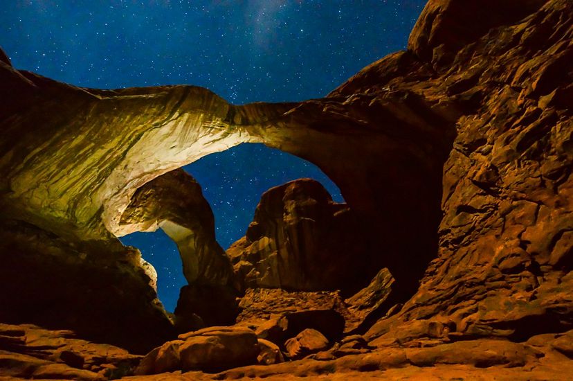 two rock arches are seen, lit against a clear starry night sky