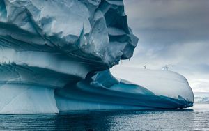 blue-white ice form stretches out over icy water with a single penguin poised near the edge of the ice over the water