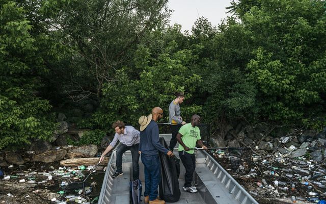 Cuatro hombres usan redes para extraer basura de la superficie del río.