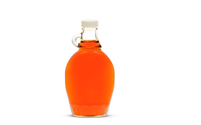 photo of a glass jug of orange-colored maple syrup, photographed on a white background