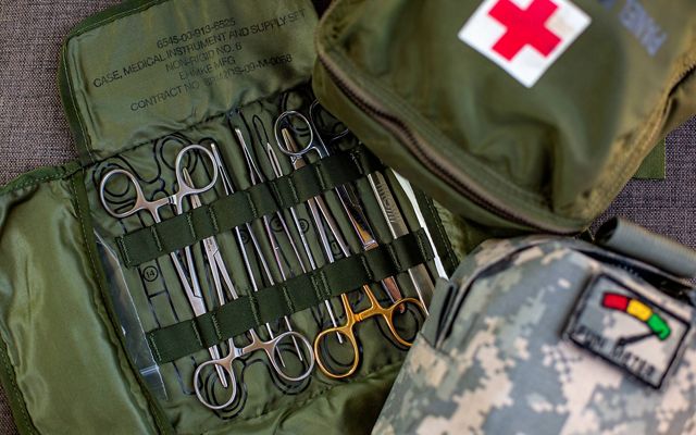 Army green medical kit is opened flat with scissors and pinchers displayed