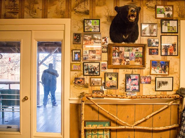 The inside of a hunting lodge with framed photos and a black bear head on the wall.