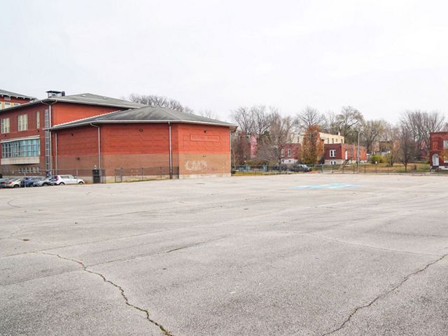 A large concrete schoolyard is adjacent to orange-painted school buildings.