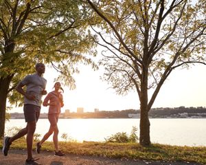 Two people jog together along a lake. Buildings are visible in the distance along the horizon.