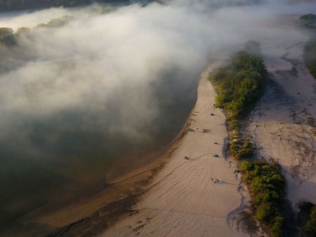Aerial view of tents on a sandy river shore.