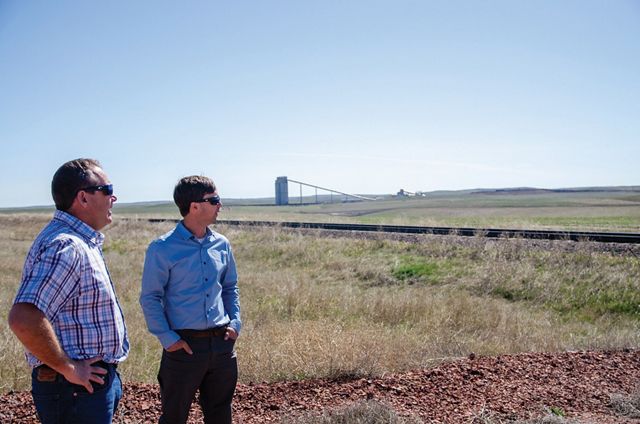 Two men stand next to each other near a wide grassy field.