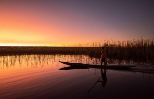 A fisherman on a canoe at sunrise.