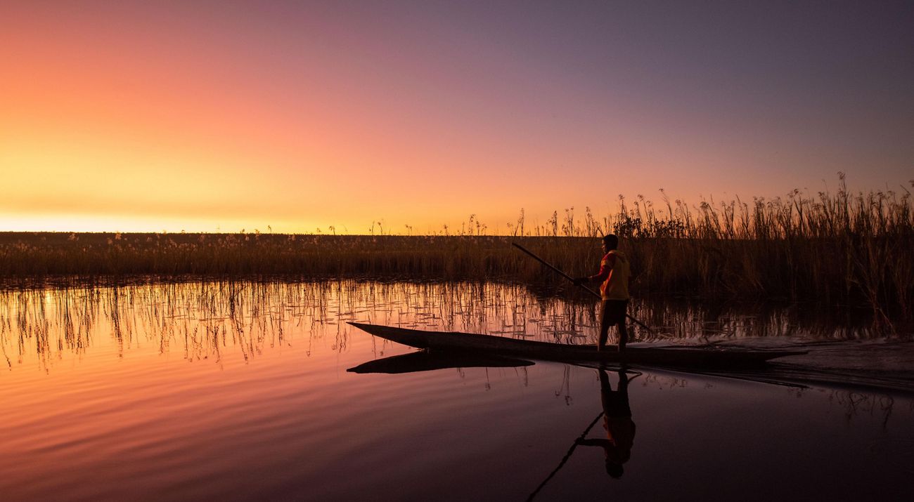 A fisherman on a canoe at sunrise.