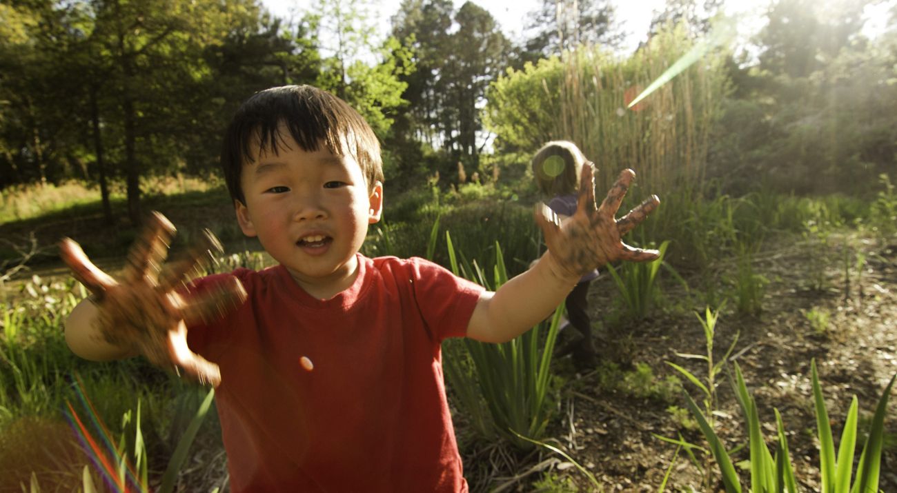 Un niño camina por un bosque mostrando sus manos con lodo