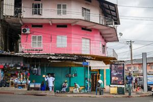 a shopkeeper stands in his doorway in a gabonese city with many power lines in the background.