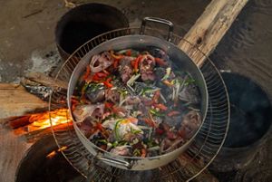 a large stockpot full of fish parts. fish heads and vegetables cooks over a wood fire.