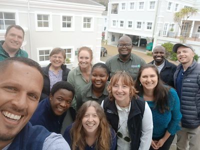 A group of 12 adults pose together smiling during daylight.