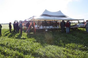 A group of farmers gather under a large tent in a field for a meeting on a sunny day in Michigan's Saginaw Valley. 