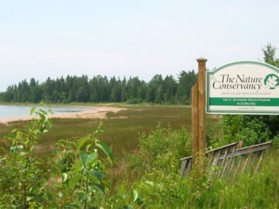 The Nature Conservancy sign on the right. On the left is shore that is sparse of plant life.