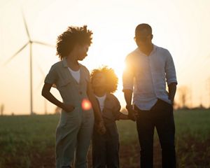Family stands in front on wind turbines at sunset.