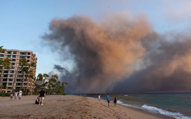 Wildfire smoke moving over a beach with a big building on the left side of the image.