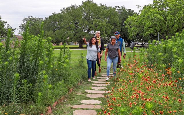 Personas caminan en un jardín con flores y arbustos abundantes.