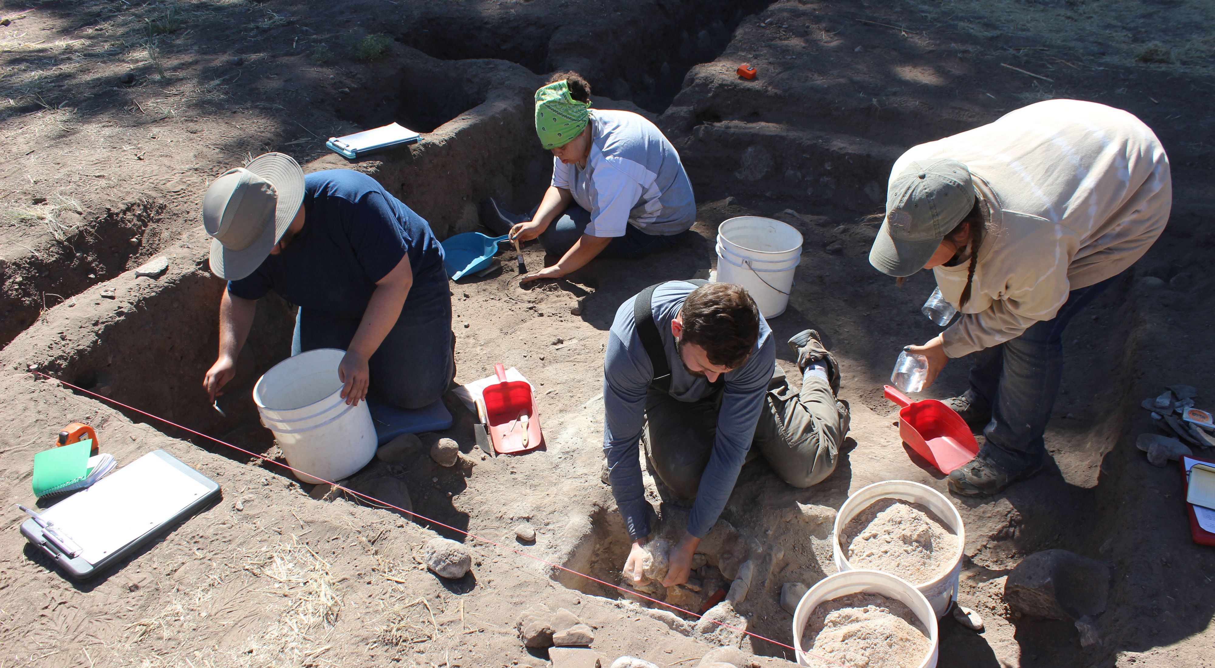 Four people with buckets excavate a site.