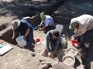 Four people with buckets excavate a site.