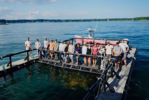 A large group of people standing on a raft overlooking oyster cages.