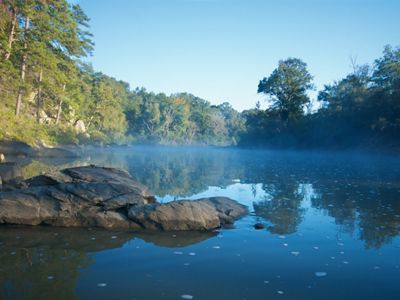 Fog rises from the waters of a slow-flowing river.
