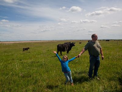 A man and his daughter standing in a field with cows in the background.
