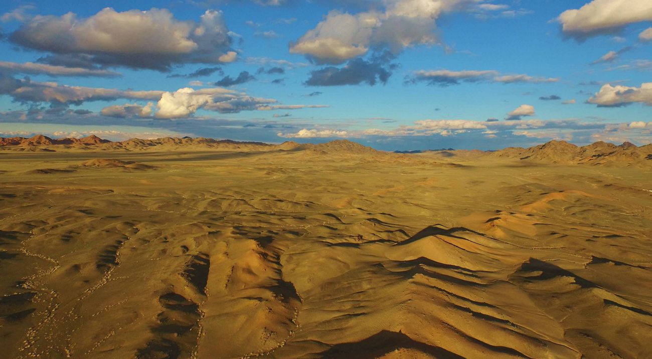 Vast expanse of rugged, arid terrain under blue sky with broken clouds.